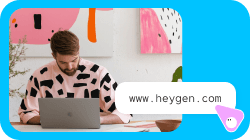 A man works on a laptop, with a chat bubble displaying 'www.heygen.com'.